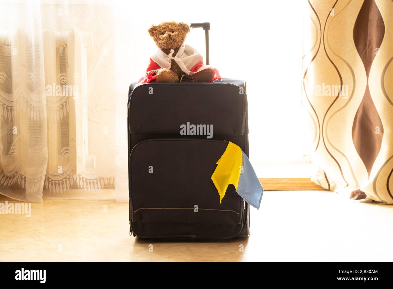 Una valigia con la bandiera della Polonia su un orso e la bandiera dell'Ucraina si trova in un appartamento in Ucraina, i rifugiati in Ucraina lasciano casa per la Polonia, guerra Foto Stock