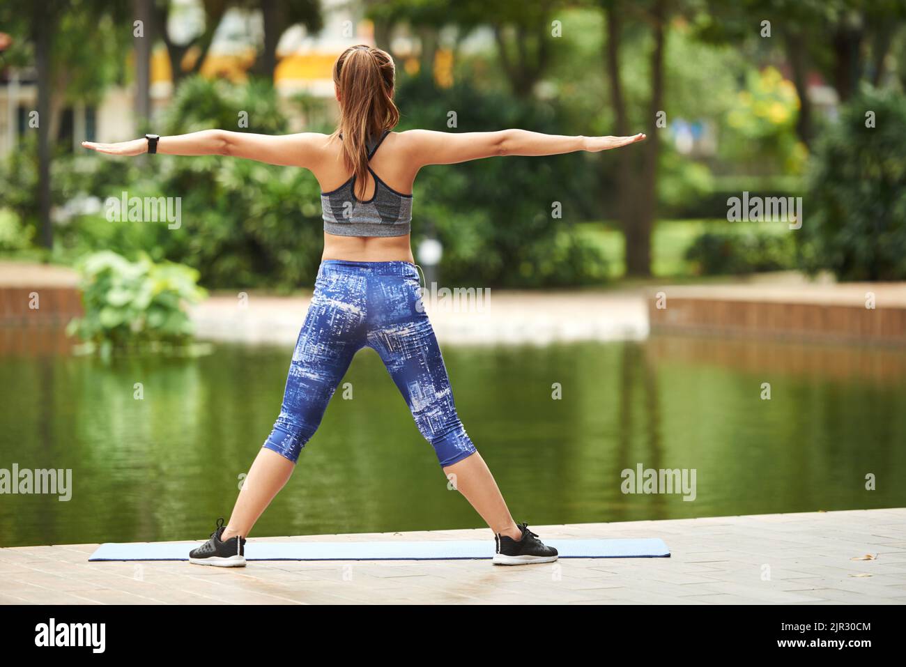 Vista posteriore della giovane donna che stretching le braccia e guardando il parco stagno . Sta godendo di buon allungamento nel suo corpo Foto Stock