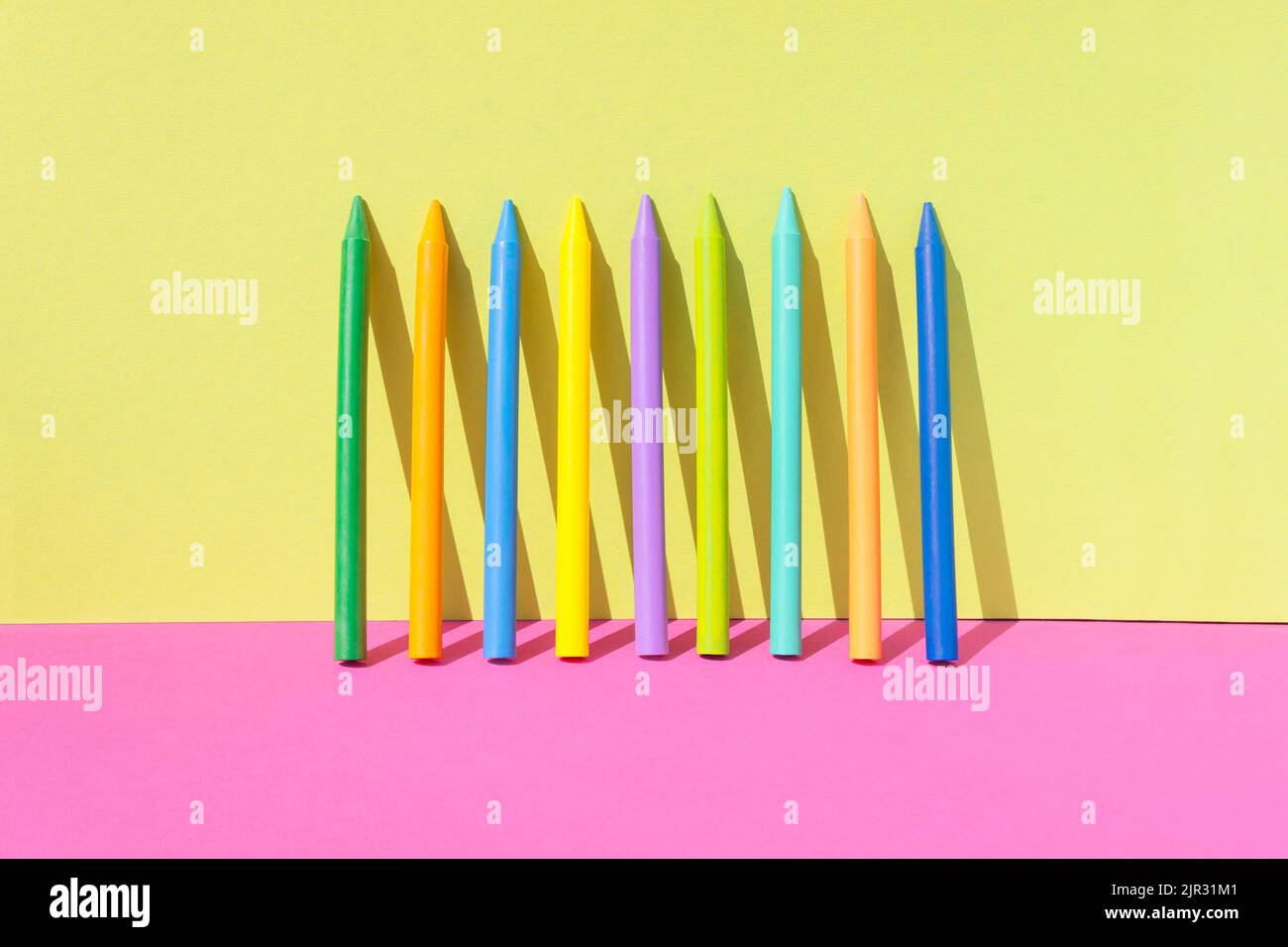 Concetto creativo di ritorno a scuola. Diversi pastelli colorati di cera isolati sullo sfondo di colore rosa e giallo. Spazio di copia. Foto Stock