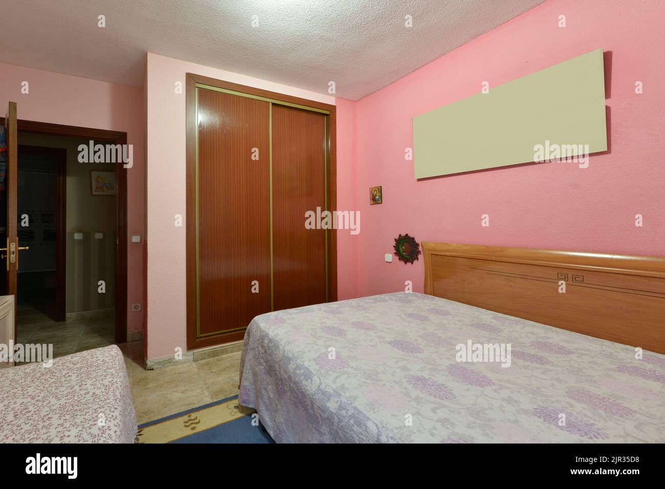 Camera con due letti, brutti copriletto, testata in legno, pavimenti in marmo color crema e armadio a muro con porte scorrevoli in legno Foto Stock