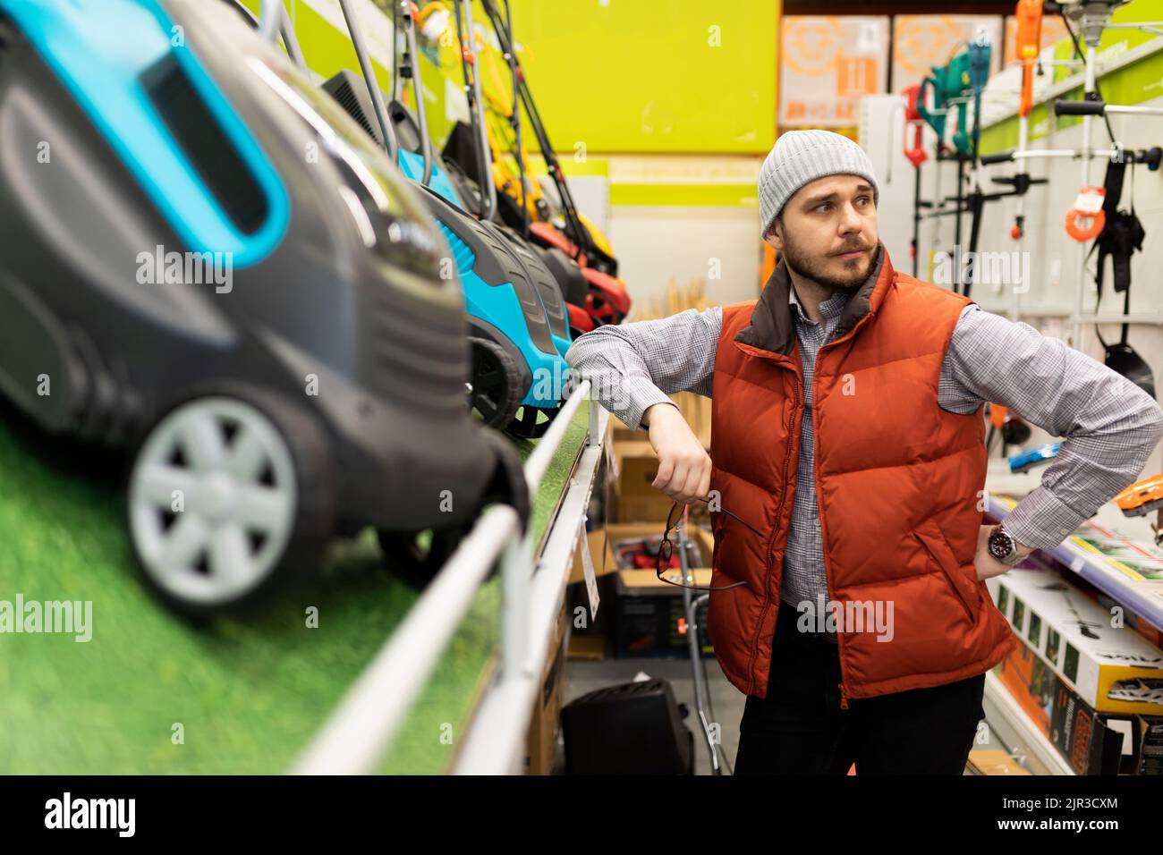 un cliente in un negozio di hardware viene determinato tra un rasaerba a benzina e un rasaerba elettrico Foto Stock