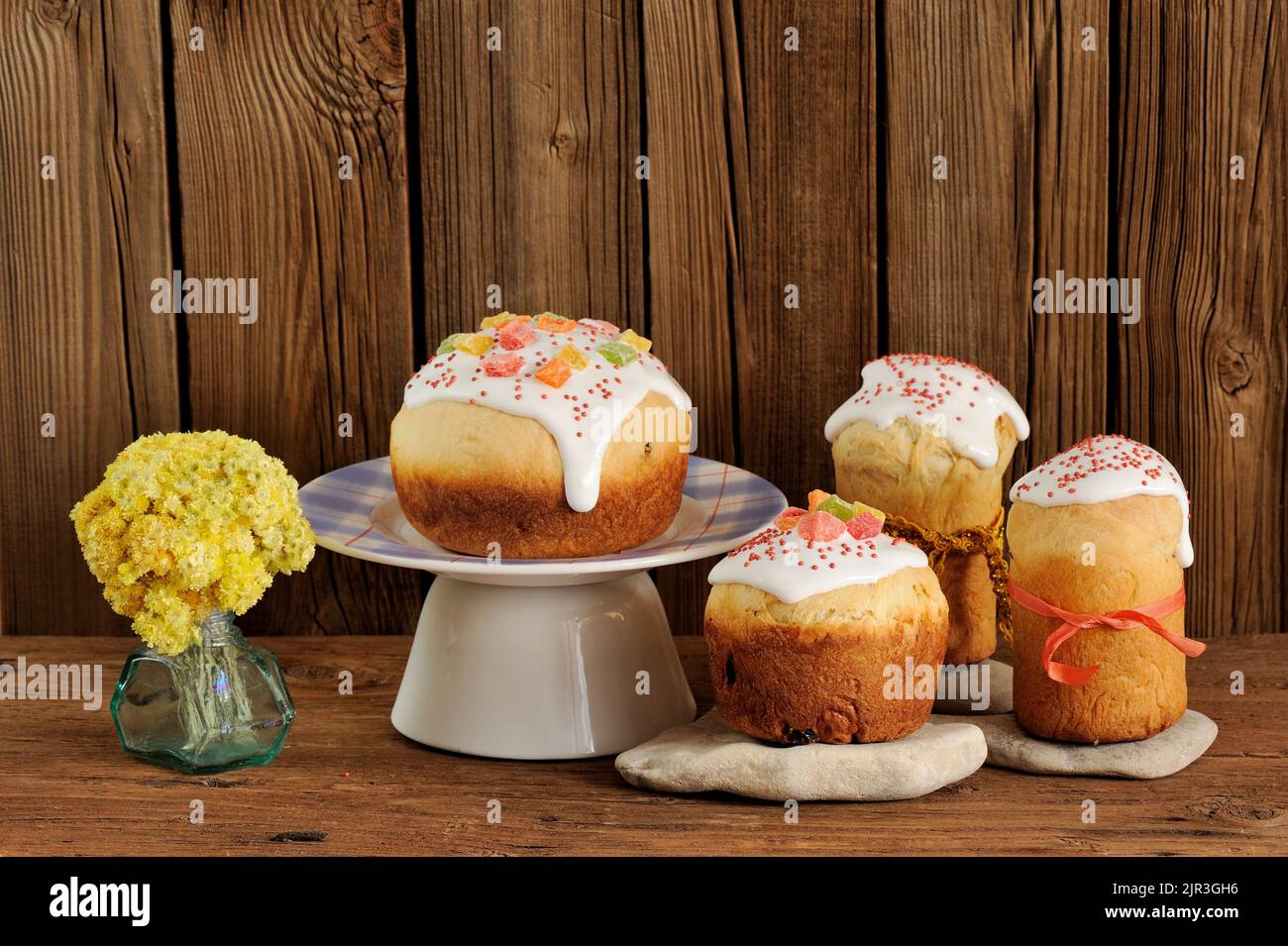 Kulich, pane dolce di pasqua russo decorato con glassa e frutta candita con fiori gialli su sfondo di legno con spazio Foto Stock