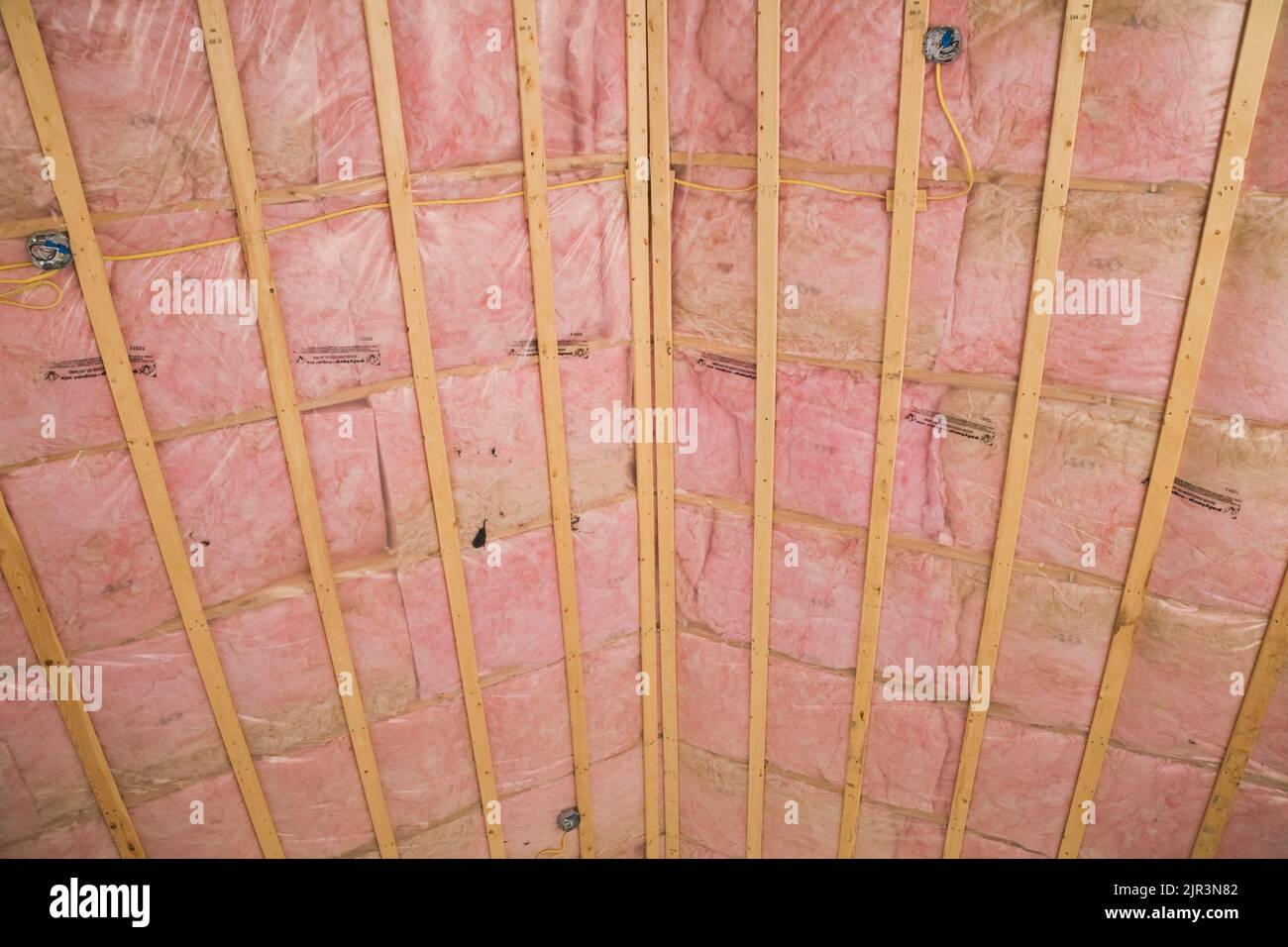 Soffitto infinito con listelli in legno e isolamento in fibra di vetro rosa a vista in casa residenziale. Foto Stock