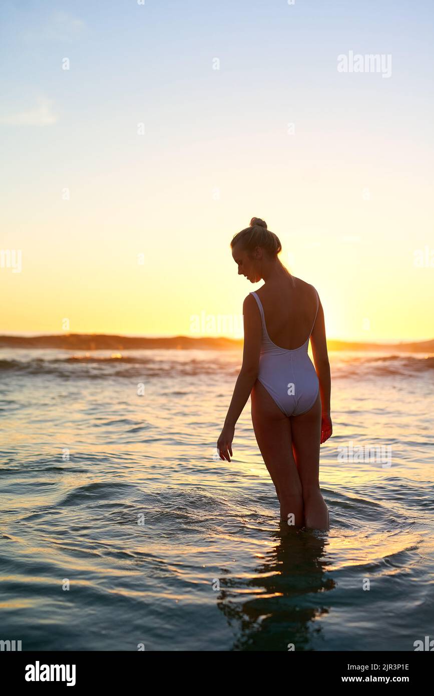 La spiaggia mi fa rivivere tutti i bei ricordi: Una giovane donna in piedi in acqua al tramonto. Foto Stock