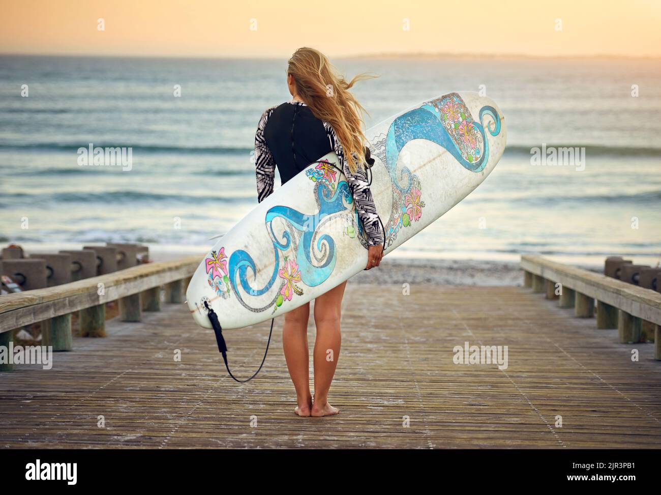 L'oceano è la sua casa. Ripresa retroversa di una giovane surfista irriconoscibile in piedi con la tavola da surf che guarda sopra l'oceano. Foto Stock