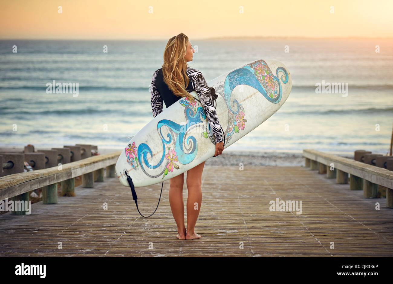 Pensieri oceanici. Ripresa da dietro di una giovane surfista attraente in piedi con la sua tavola da surf che guarda sopra l'oceano. Foto Stock