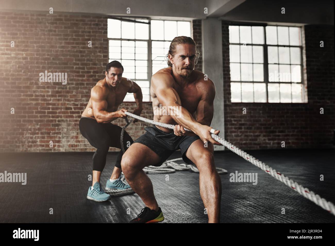 Youre ottenere più forte con ogni secondo. Due giovani uomini muscolari che tirano su una corda in una palestra. Foto Stock
