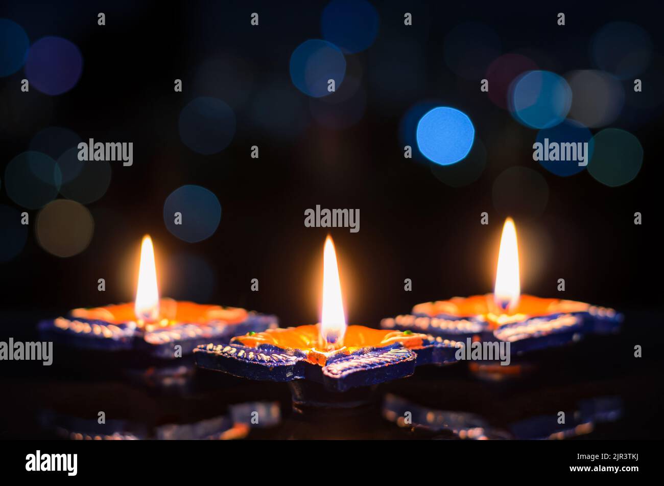 Fuoco selettivo sulla fiamma delle prime lampade diya in argilla illuminate su sfondo scuro con colorate luci bokeh. Concetto di festival Diwali. Foto Stock
