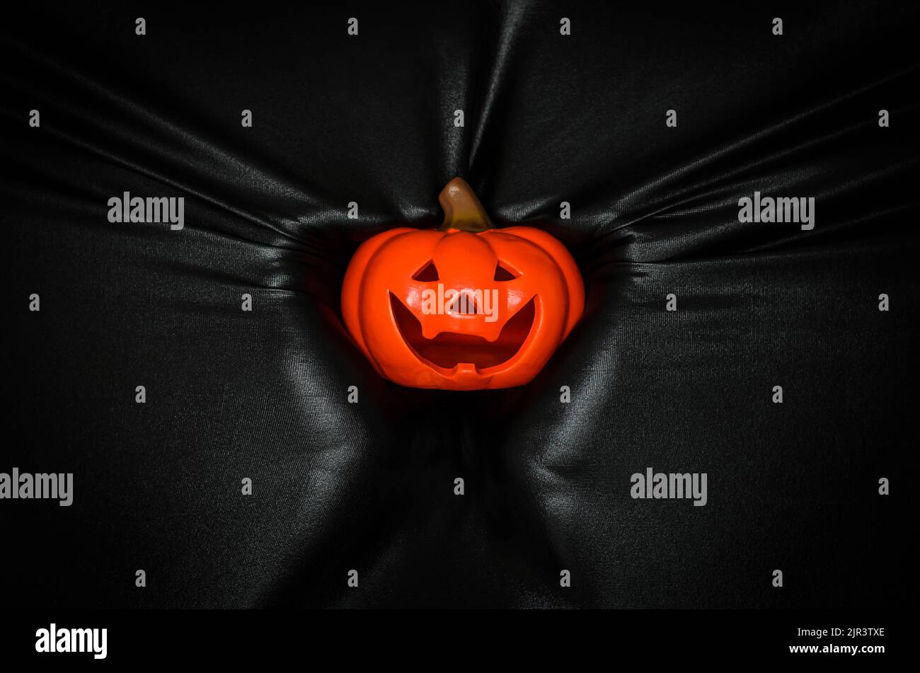 Zucca di Halloween tenendo premuto a mano attraverso sfondo di tessuto nero. Concetto di festa di Halloween. Foto Stock