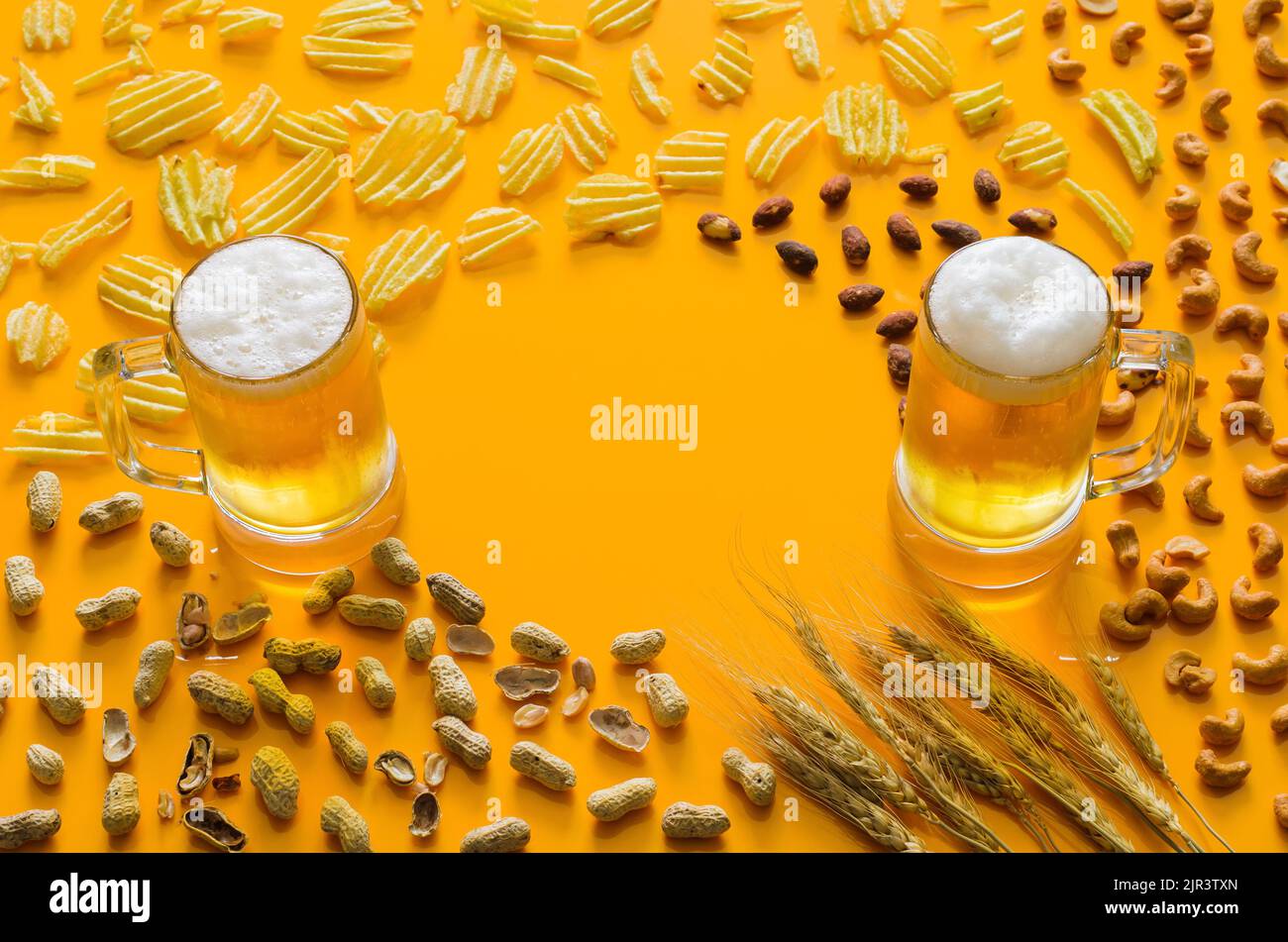 Due bicchieri di birra con patatine fritte e noci su sfondo giallo per l'Oktoberfest Concept. Foto Stock