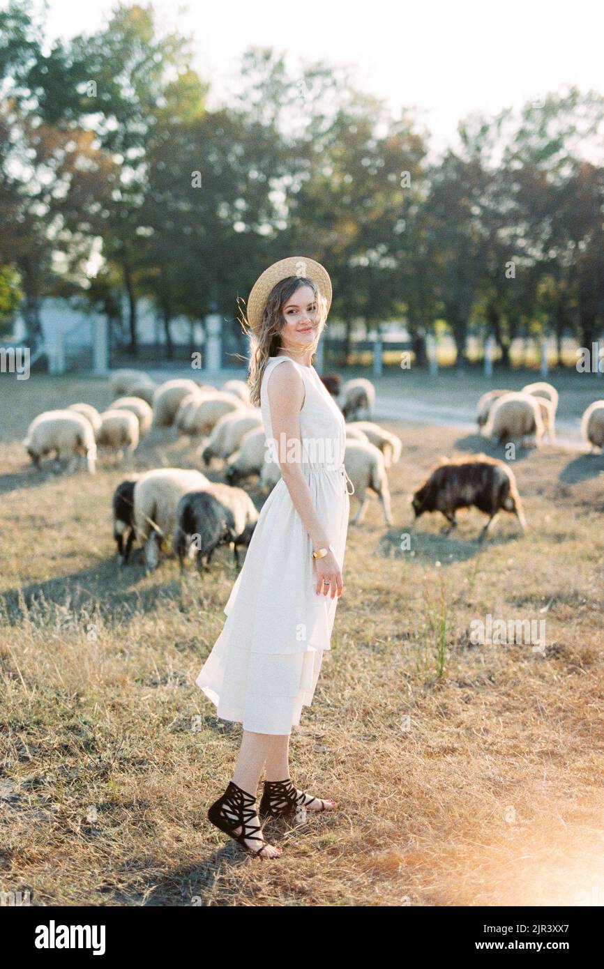 Ragazza sorridente in un cappello di paglia si trova vicino a pecore al pascolo Foto Stock