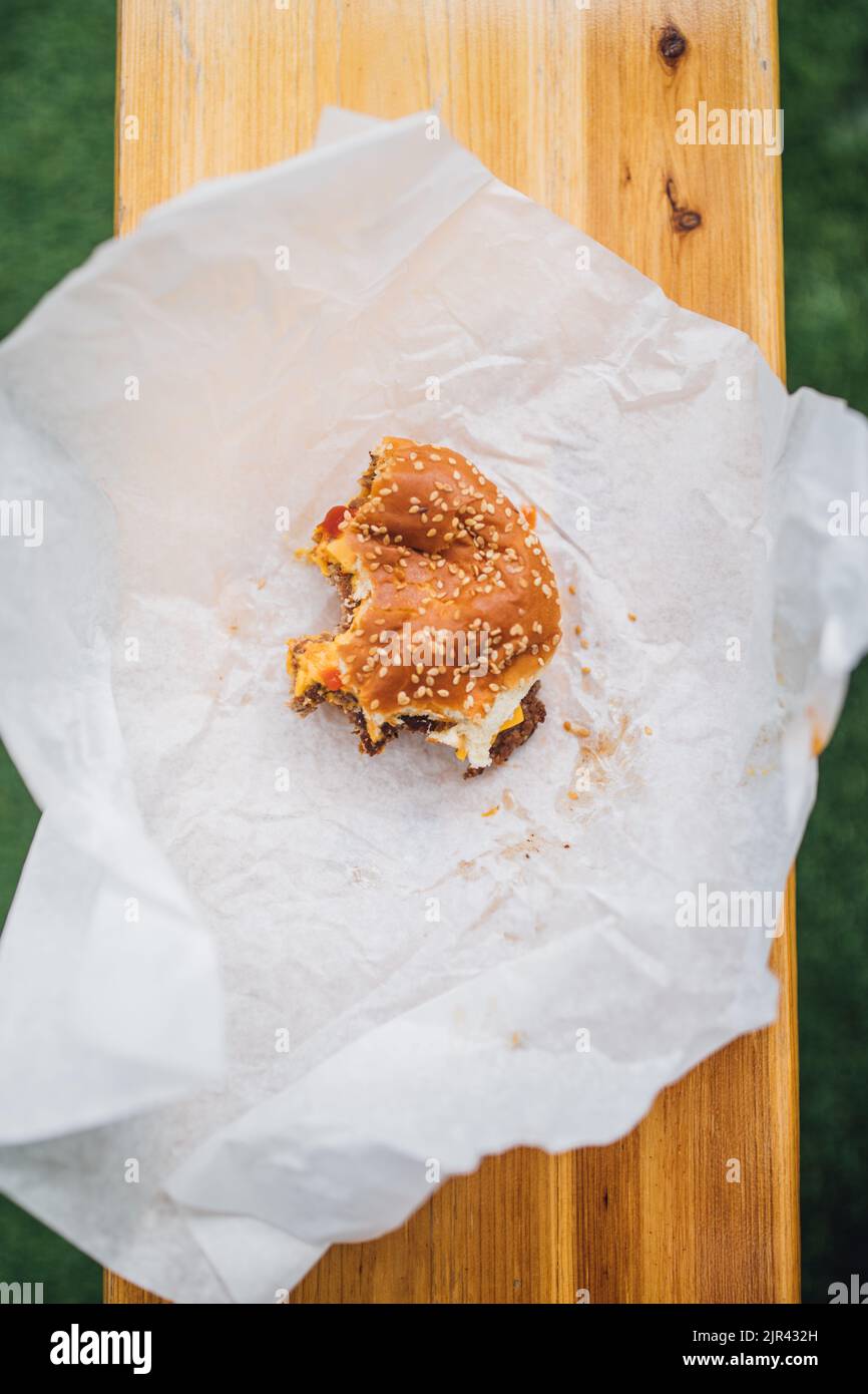 cheeseburger mangiato a metà con panino di sesamo su carta bianca Foto Stock