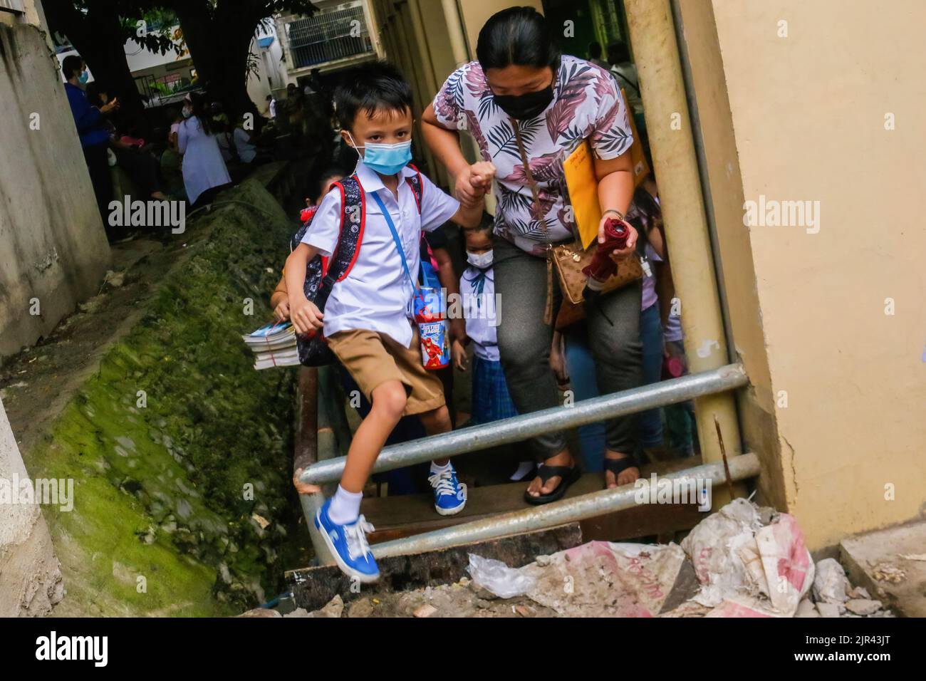 Un genitore guida il suo bambino mentre lottano per passare su una recinzione di metallo per ottenere attraverso la loro classe designata. Le Filippine iniziano le lezioni di persona dopo 2 anni di scuola virtuale a causa della pandemia. Il Dipartimento dell'Educazione (DepEd) ha detto che ci sono 27.691.191 studenti iscritti per l'anno scolastico 2022-2023. Il 19% degli studenti nelle Filippine è completamente vaccinato e il 20% ha ricevuto solo la prima dose di vaccino COVID-19, ha affermato DedePed. Il protocollo del dipartimento è, se ci sono casi di COVID-19 o alcuni studenti che sperimentano sintomi simil-influenzali, si sposteranno definitivamente da in-p Foto Stock