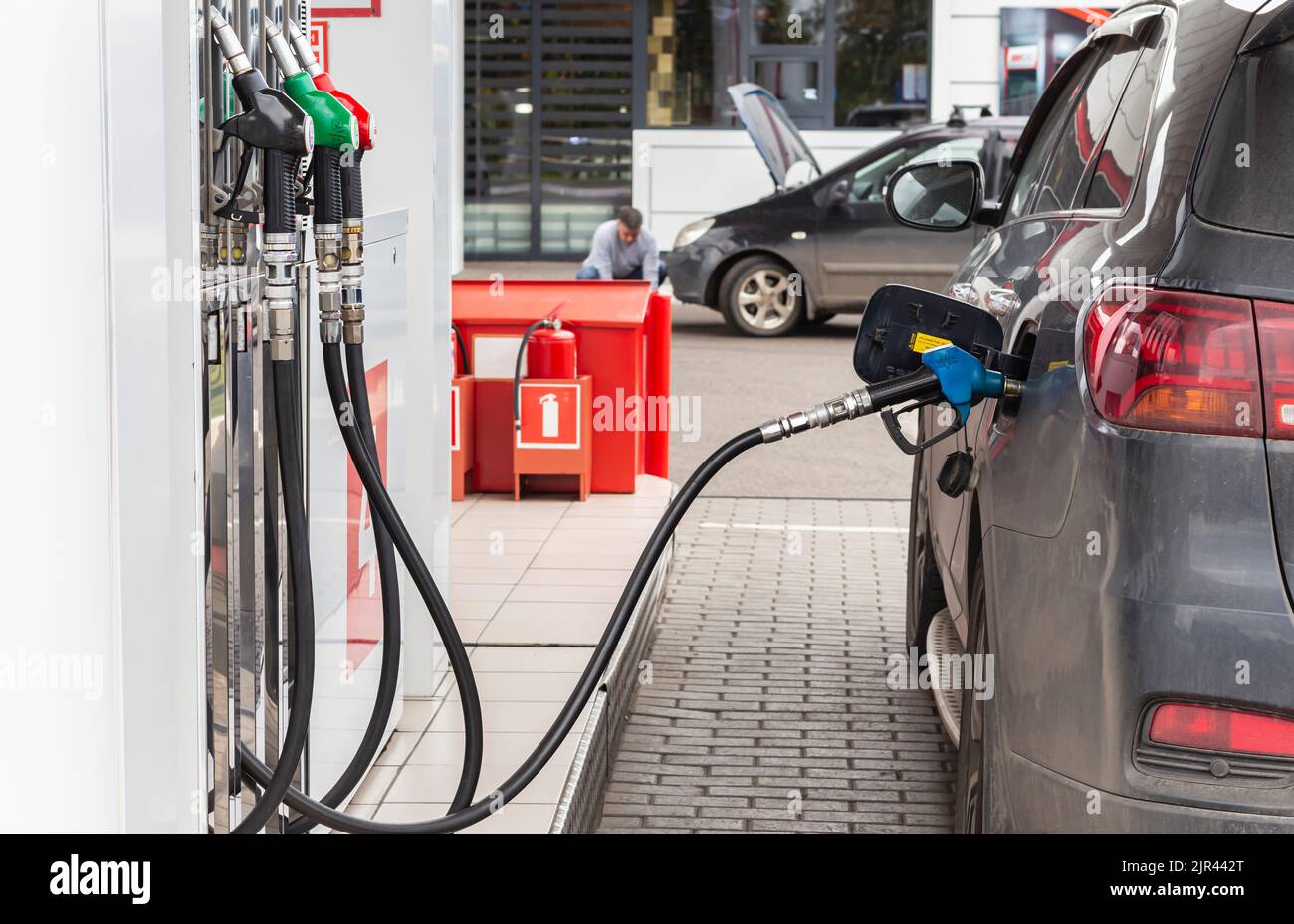 Stazione di rifornimento carburante. Maneggiare l'ugello del combustibile per effettuare il rifornimento. Auto nera alimentata da. Adulto attraente uomo caucasico servizi la sua auto, selecteve fuoco. Foto Stock