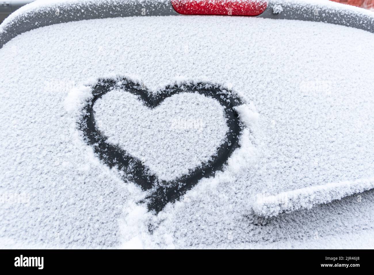 Cuore di neve sul finestrino dell'auto con spazio per la copia. Cuore segno in fiocchi di neve freschi. Simbolo di forma del cuore disegnato sul vetro innevato dell'automobile. Concetto di amore. San Valentino Foto Stock