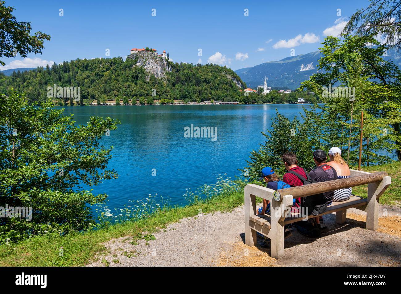 Bled, Slovenia - 18 luglio 2022: Famiglia di quattro persone goditi la vista panoramica del lago di Bled e del castello di Bled da una panchina, popolare destinazione turistica. Foto Stock