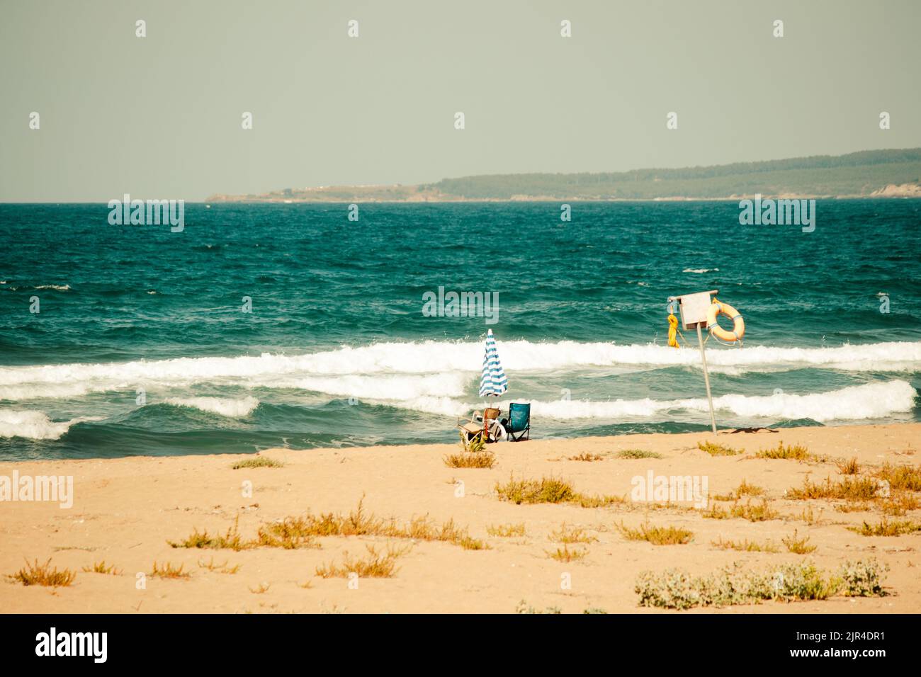 Foto di spiaggia deserta con colori vintage. Costa vuota fuori cartello di avvertimento con ombrellone e due sedie da campeggio. Zona del poggiatesta lontana dalle persone. Foto Stock