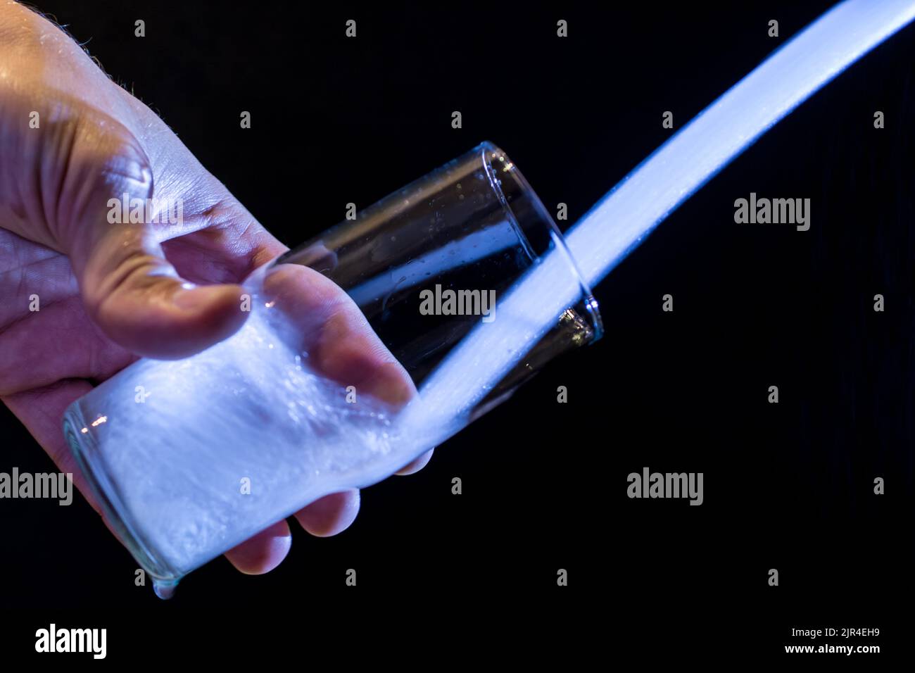 L'acqua scorre in un bicchiere di vetro di fronte allo sfondo nero Foto Stock