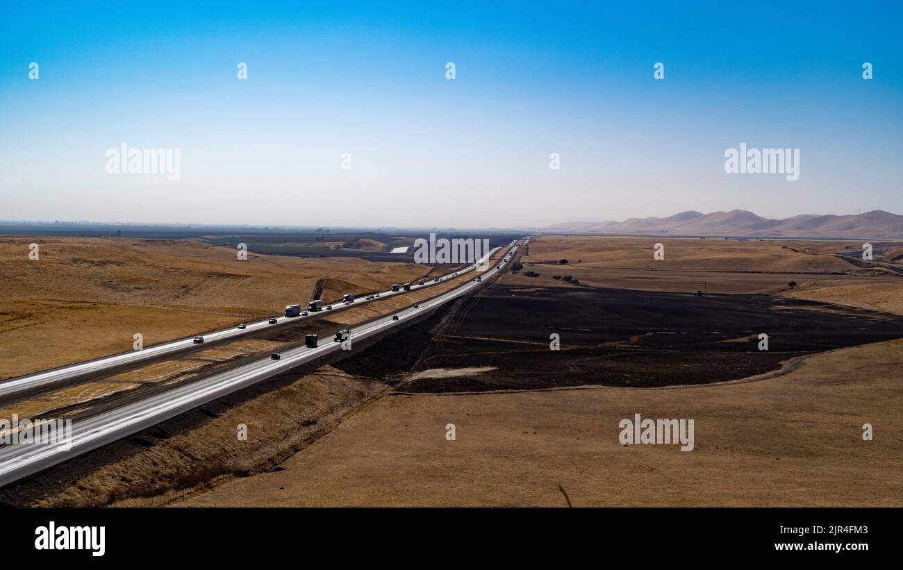 Autostrada che attraversa un terreno agricolo bruciato dal sole Foto Stock