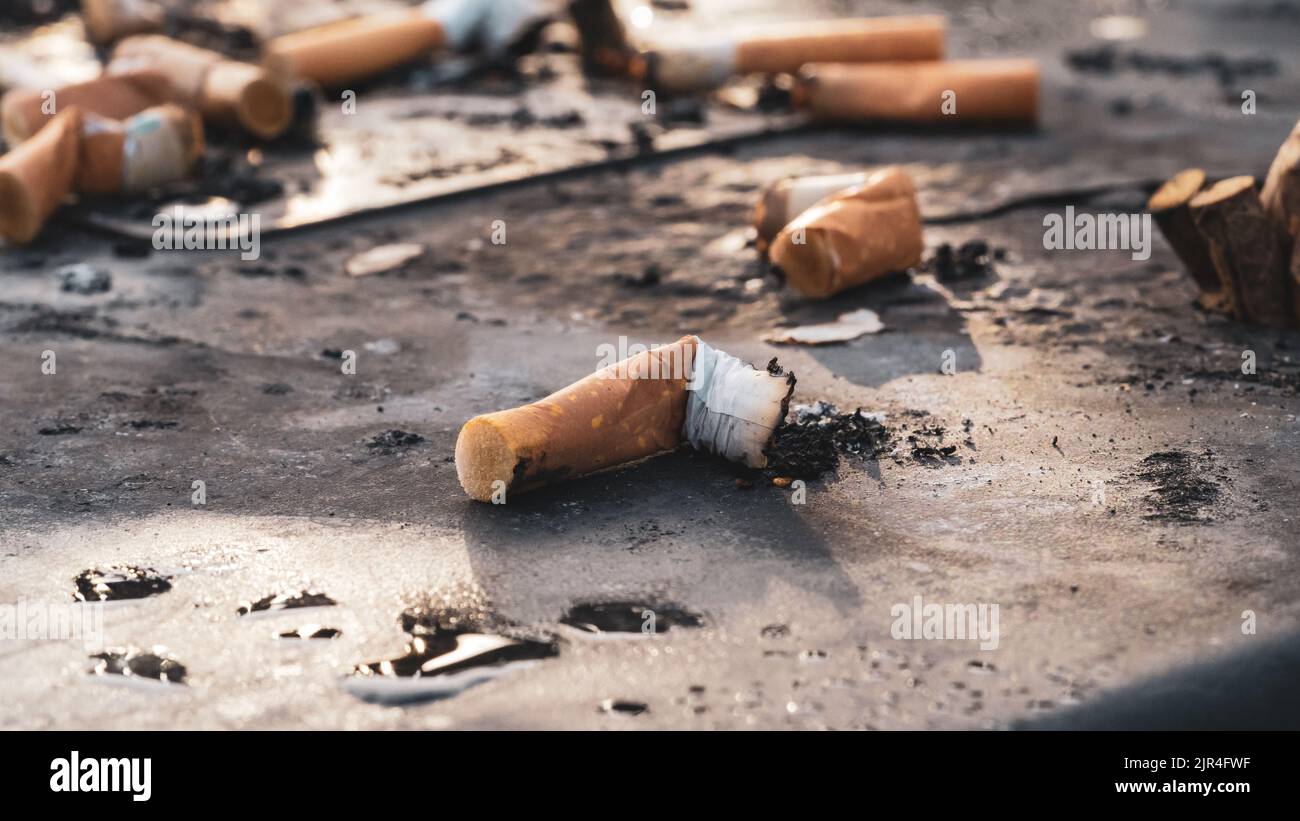 I mozziconi di sigaretta usati gettati sulla superficie sporca del posacenere Foto Stock