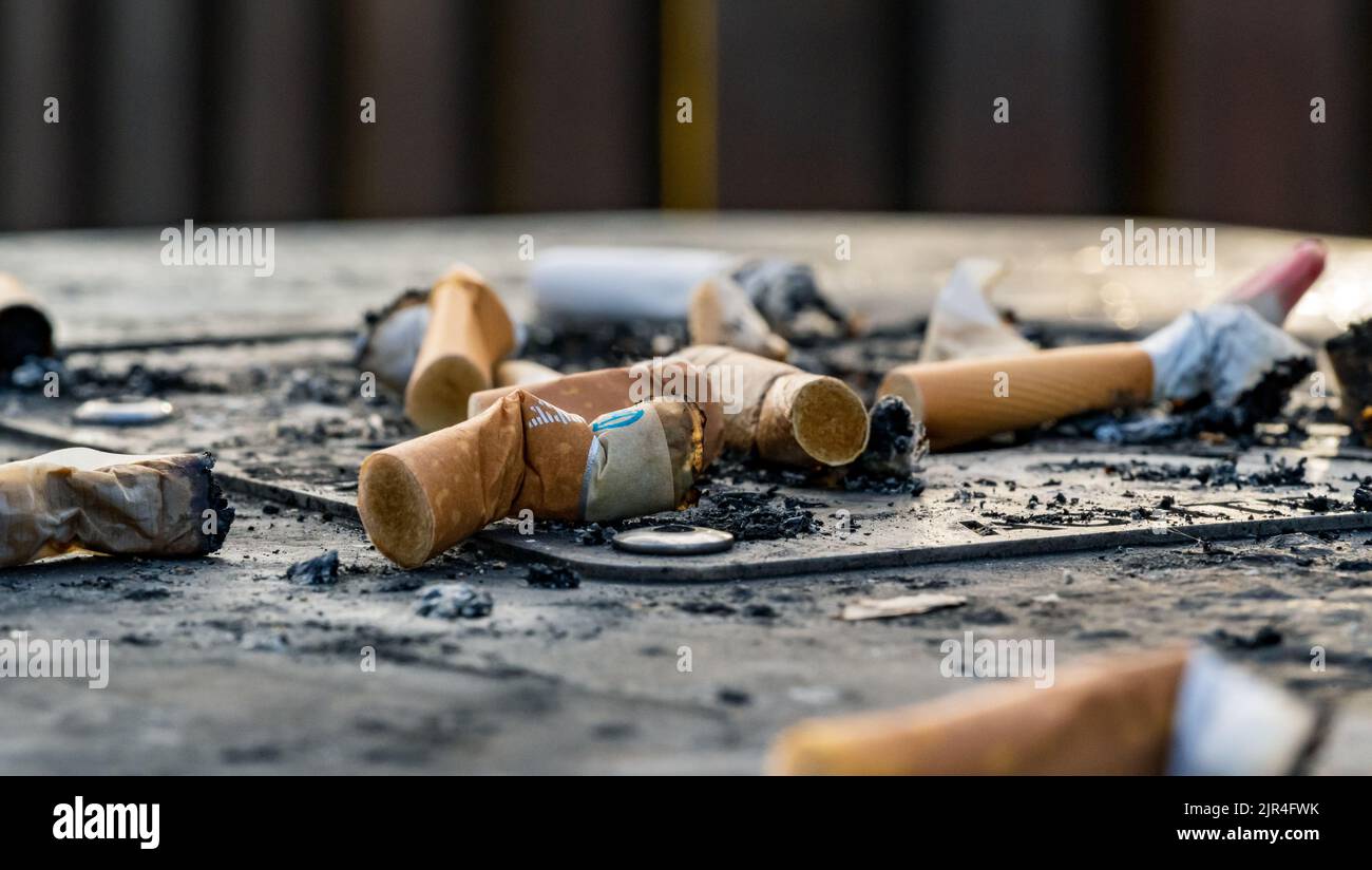 I mozziconi di sigaretta usati gettati sulla superficie sporca del posacenere Foto Stock