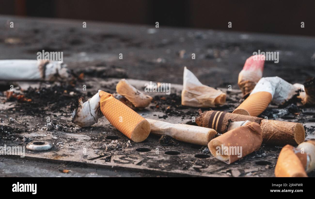 I mozziconi di sigaretta usati gettati sulla superficie sporca del posacenere Foto Stock