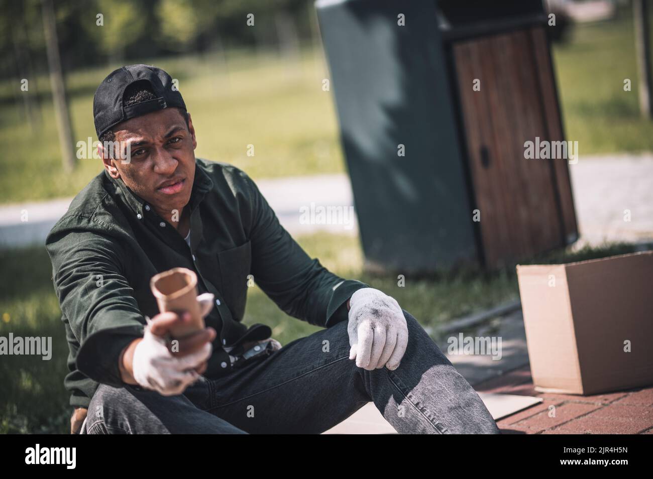 Uomo seduto a terra che tiene la mano alla fotocamera Foto Stock