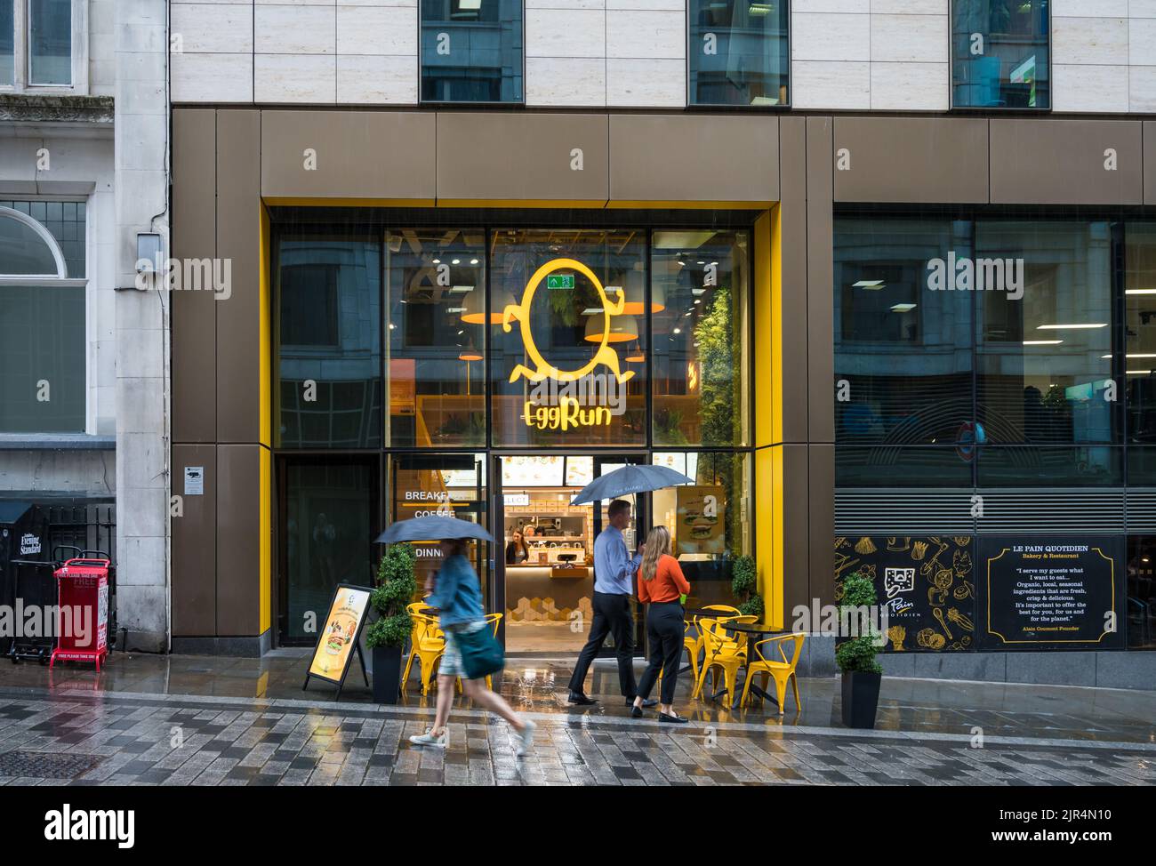Le persone con ombrelli allevati in una giornata di pioggia passeranno da Eggrun, un ristorante e da asporto su Fish Street Hill, City of London, England, UK Foto Stock