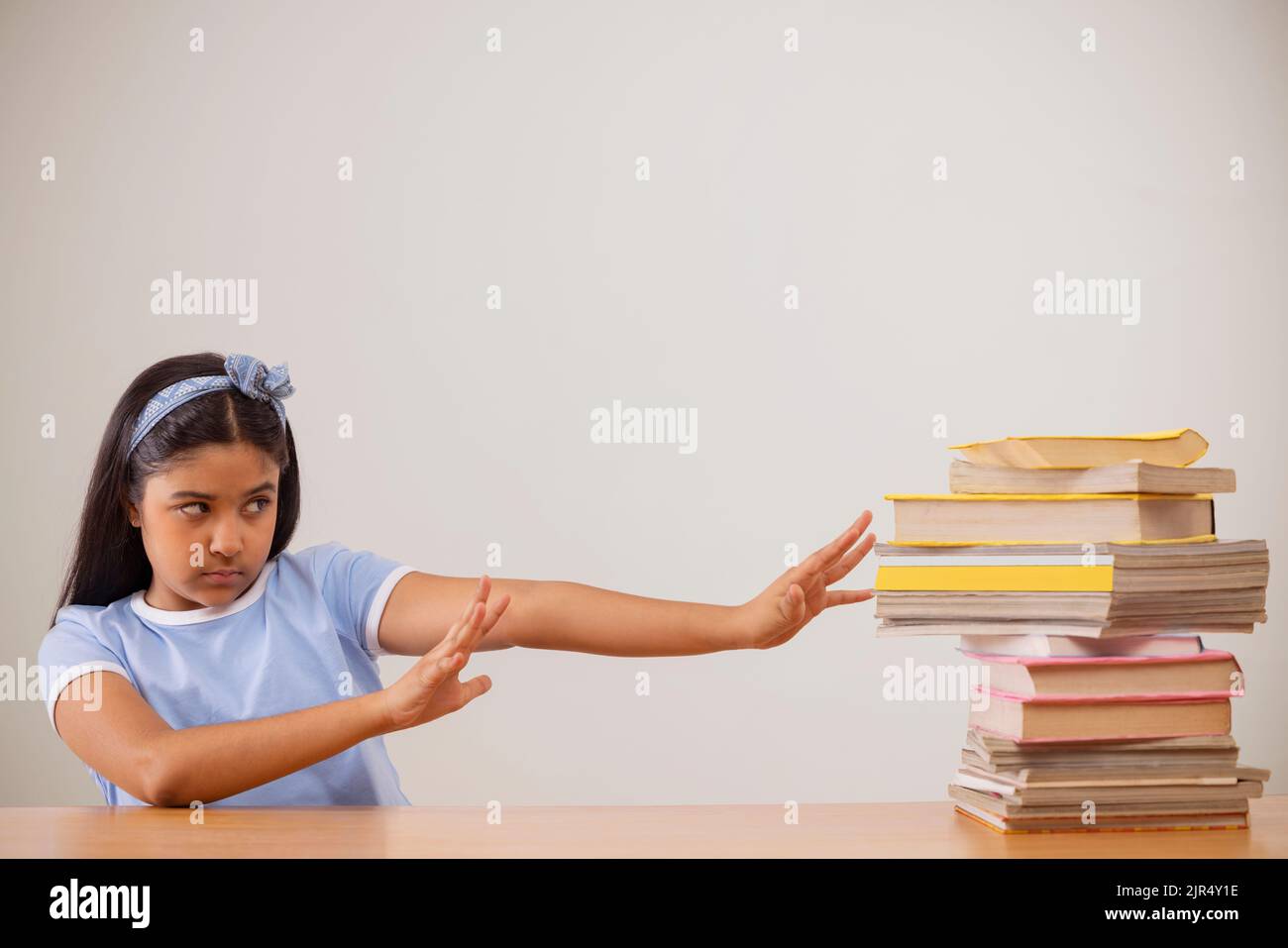 Ragazza che esprime riluttanza mentre si siede accanto a una pila di libri Foto Stock