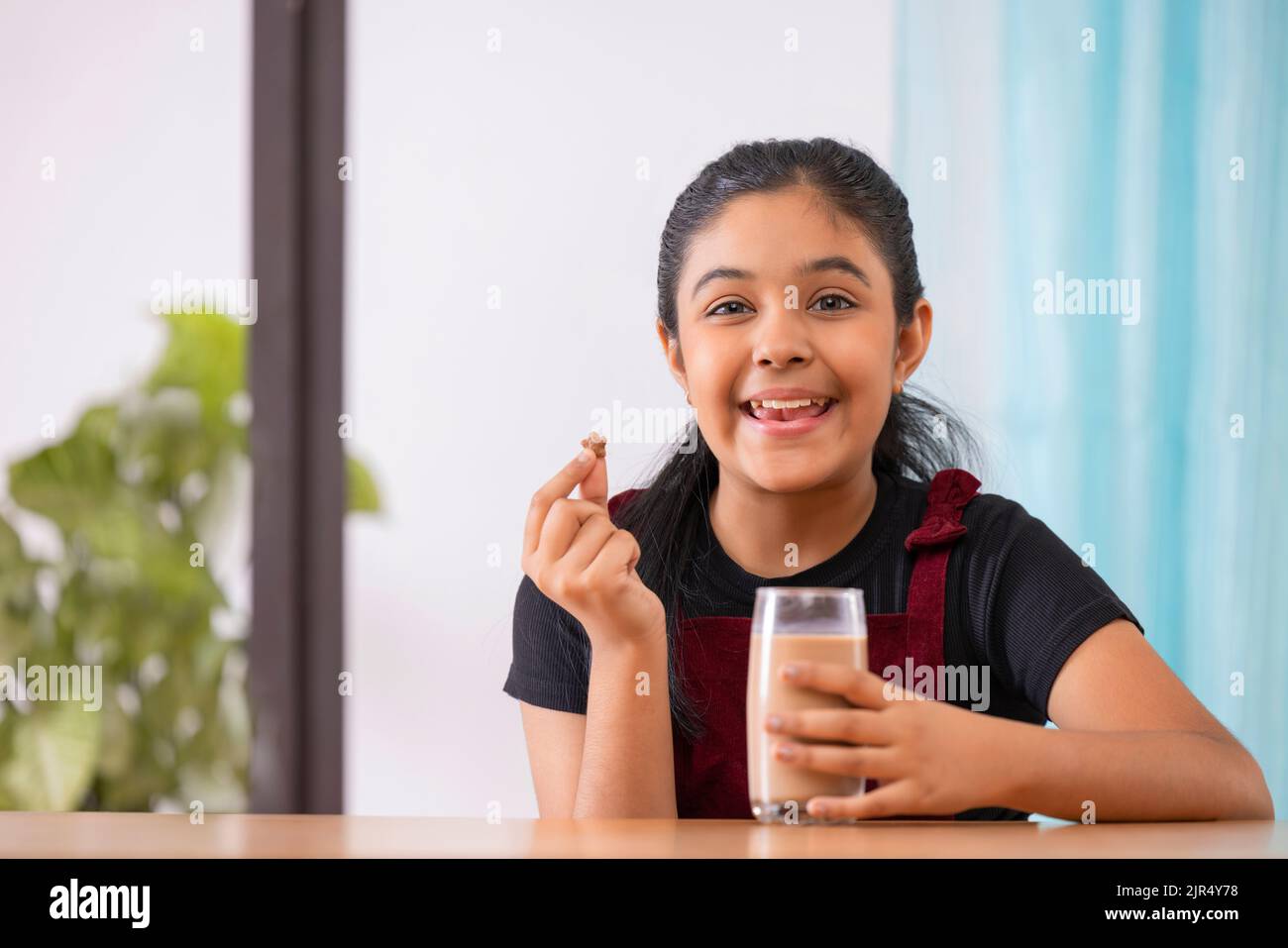 Ritratto di allegra bambina che ha la colazione con cereali e cioccolato milkshake a casa Foto Stock
