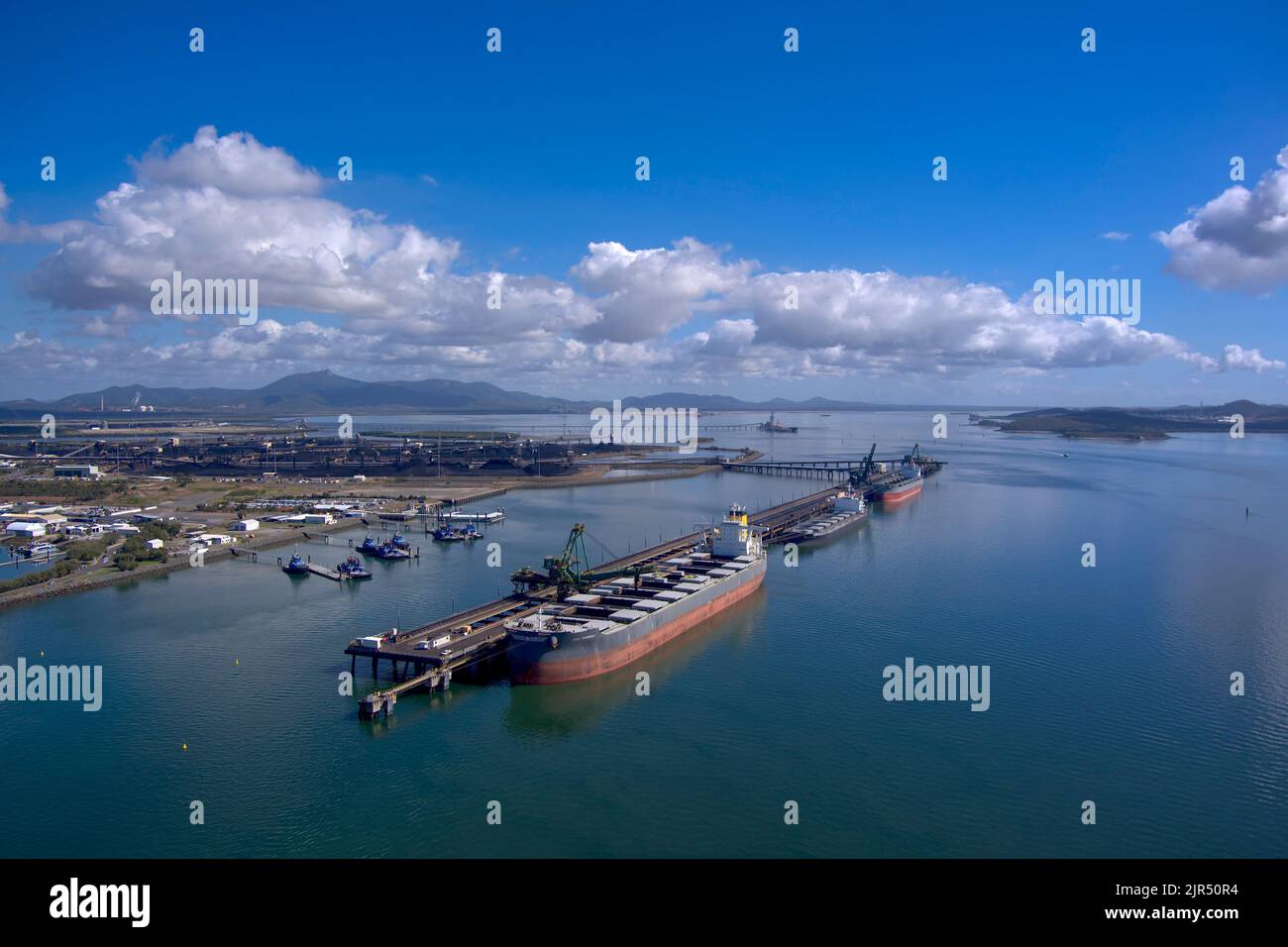 Vista aerea delle navi da carico attraccate in un trafficato porto industriale con cieli limpidi e acque blu calme. Gladstone, Queensland, Australia Foto Stock