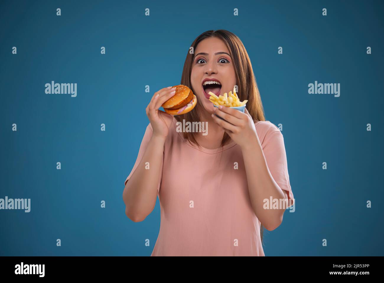 Ritratto di una donna affamata che mangia hamburger e patatine fritte insieme Foto Stock