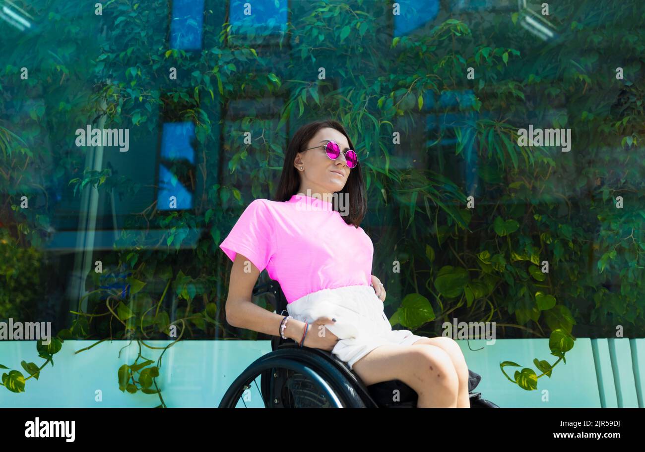 Giovane donna adulta in sedia a rotelle seduta di fronte al verde Foto Stock