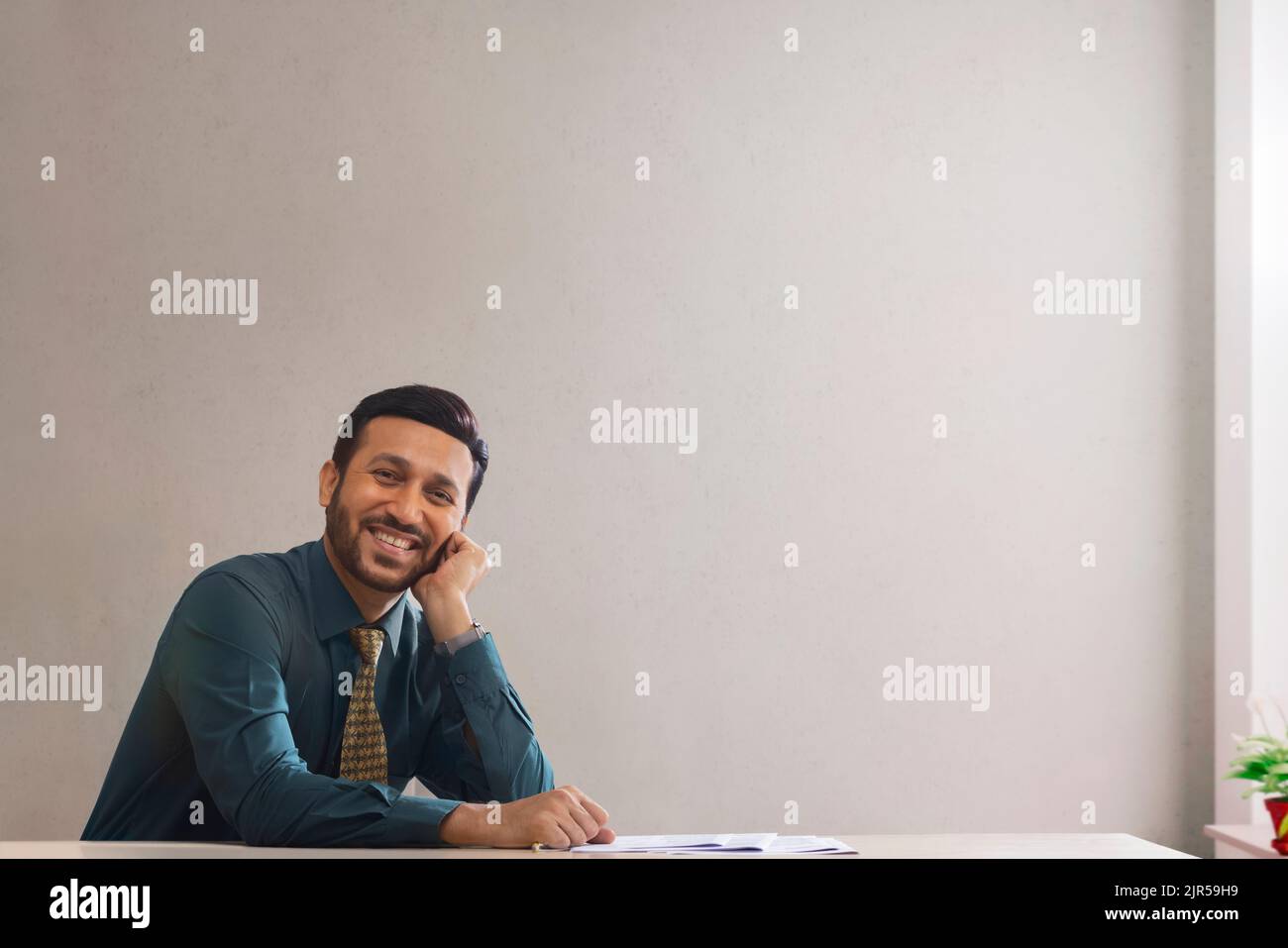 Un dipendente aziendale felice nell'abbigliamento formale seduto con mano sul viso. Foto Stock