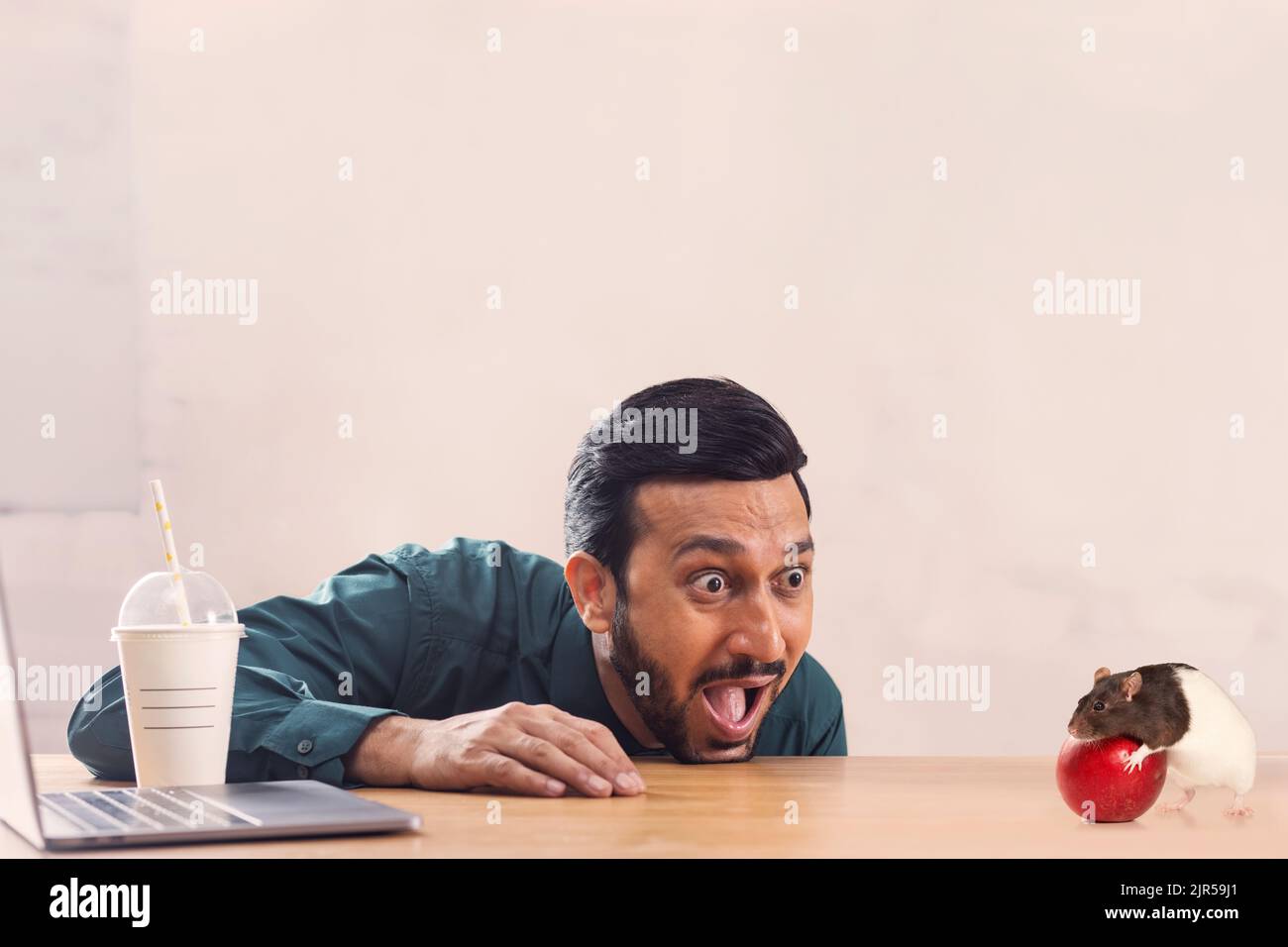 Un dipendente aziendale con notebook e drink sorpresi guardando un mouse nibbling una mela. Foto Stock