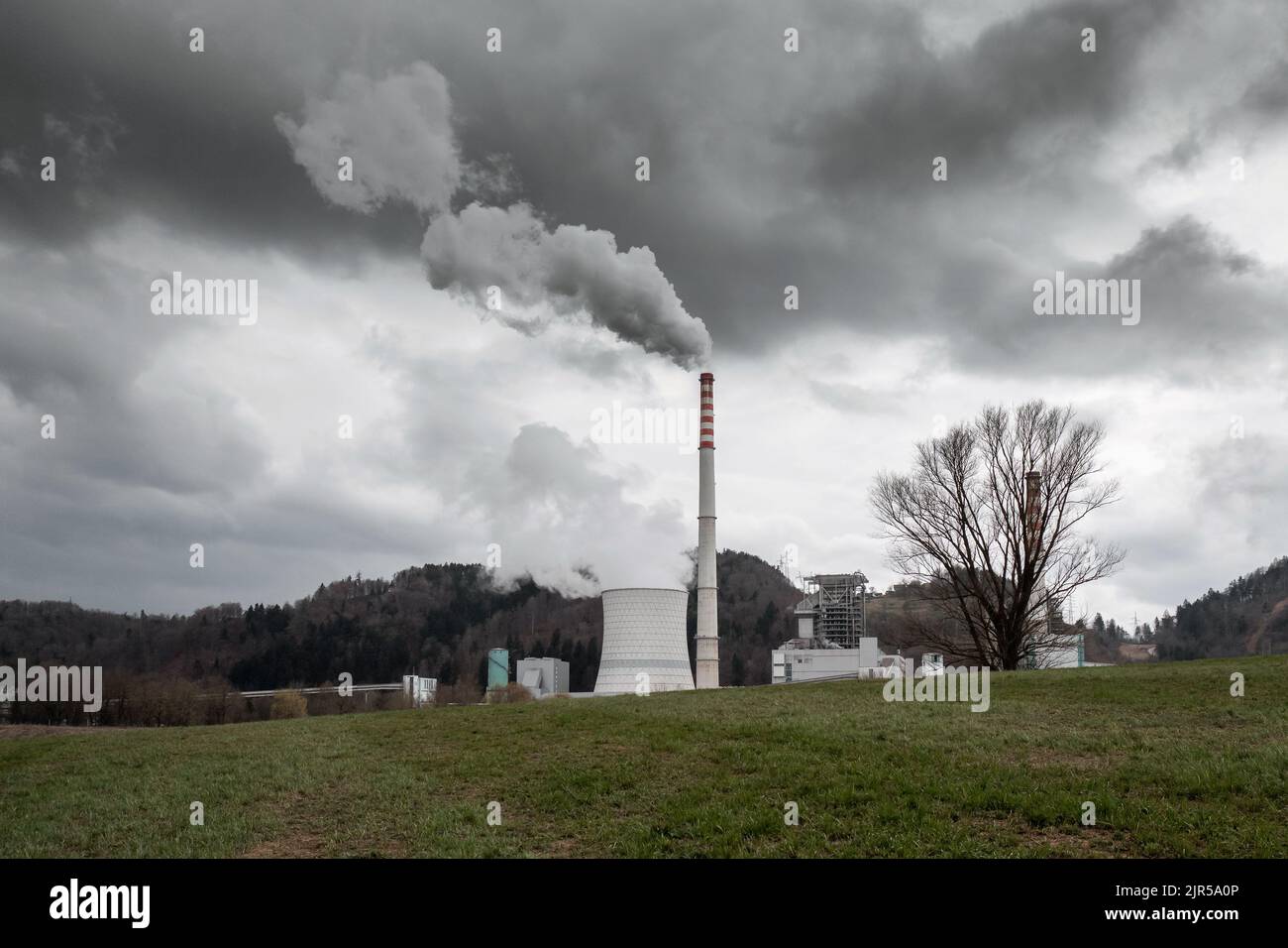 Torre di raffreddamento e camino di centrale termica con denso fumo bianco e grigio che sale nel cielo Foto Stock