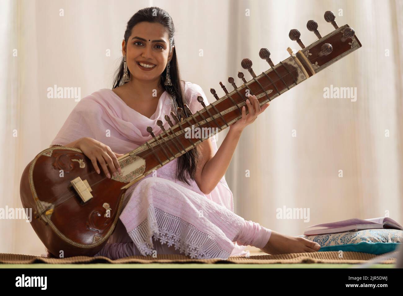 Giovane musicista femminile che suona Sitar a casa Foto Stock