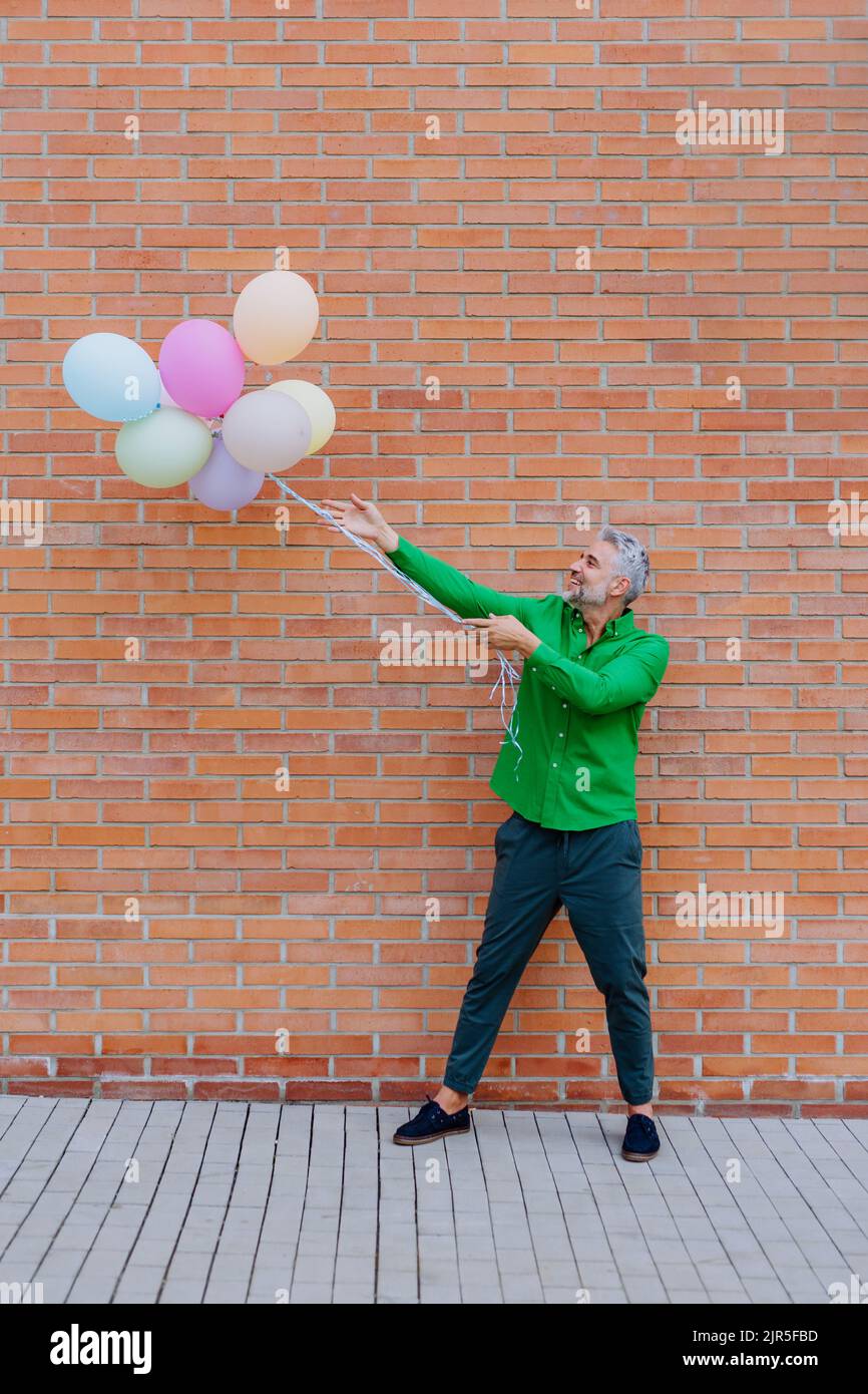 Ritratto divertente di felice energico uomo d'affari maturo tenendo palloncini in strada, sensazione di libertà, lavoro vita equilibrio concetto. Foto Stock
