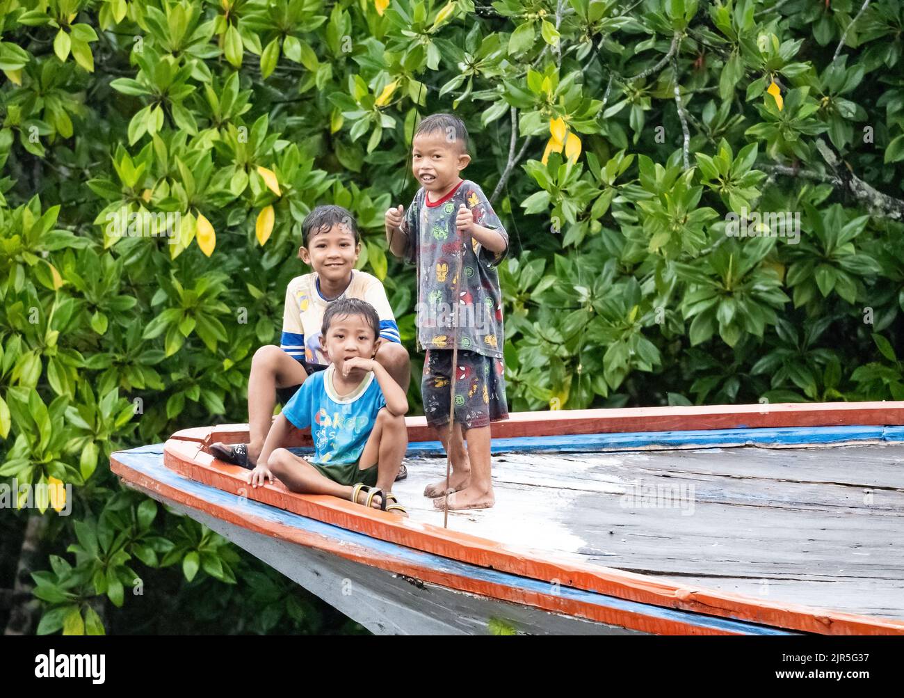 Tre ragazzi indonesiani giocano su una barca da pesca. Sulawesi, Indonesia. Foto Stock