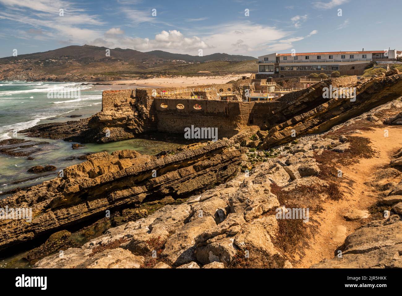 Rocce sciolte e onde persistenti sulla costa atlantica portoghese con un hotel terrazzato tra le rocce Foto Stock