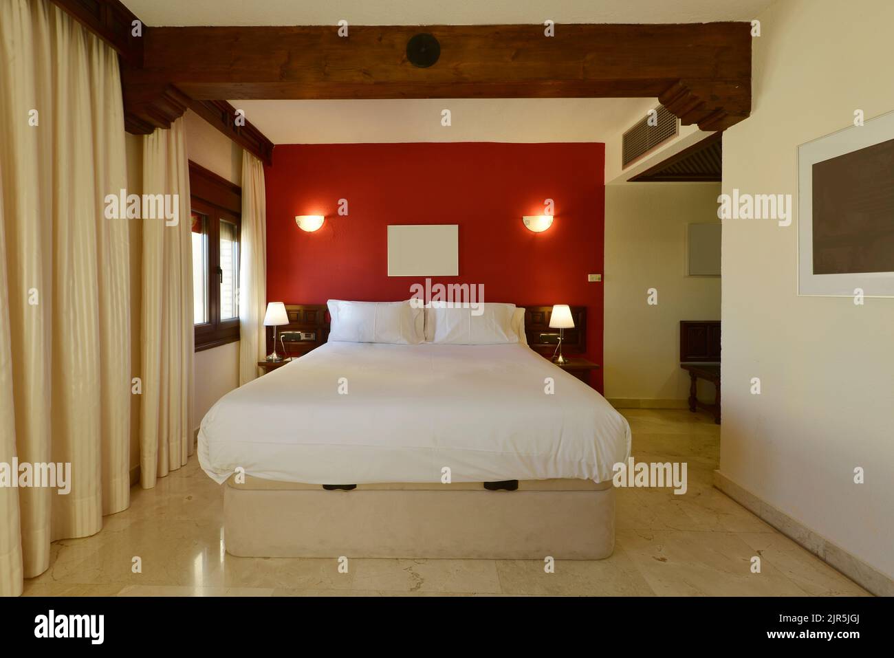 Camera con letto matrimoniale con pareti rosse, pavimenti in marmo crema, tende abbinate e travi in legno Foto Stock