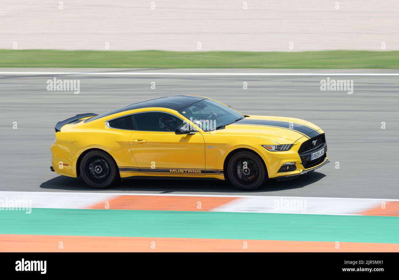 Una splendida Ford Mustang gialla con una striscia nera che corre intorno a una pista da competizione Foto Stock