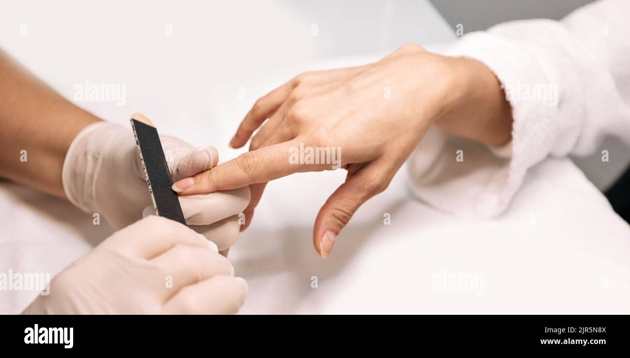 Manicurista che archiva le unghie della donna al suo tavolo di lavoro. Processo di cura delle unghie, primo piano Foto Stock