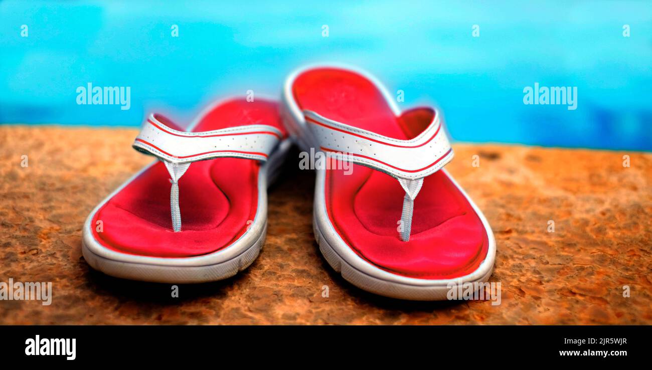 Paia di sandali rossi infradito accanto alla piscina limpida con acqua fresca blu rinfrescarsi Foto Stock