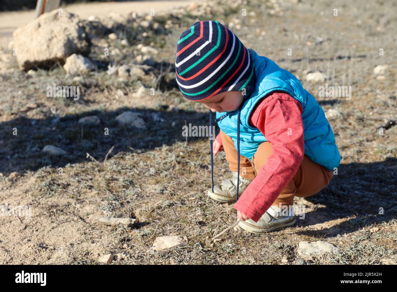 Bambino che gioca con bastone di legno e roccia su un campo. Collegamento natura. Foto Stock