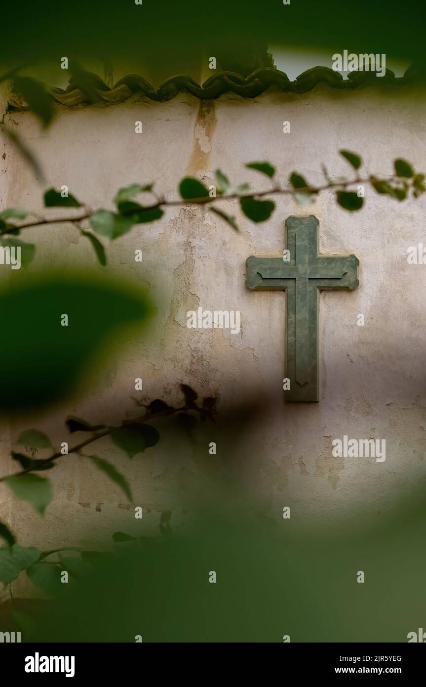 Religione incrociata. Simbolo. Culto. Croce su muro usurato tra vegetazione, pianta fuori fuoco e piastrelle in cima, messico Foto Stock