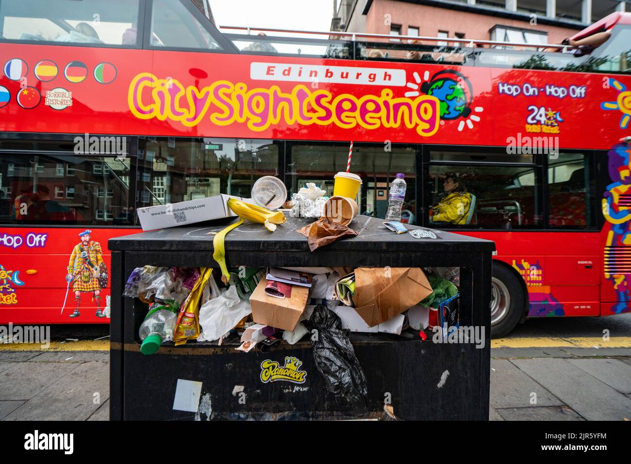 Edimburgo, Scozia, Regno Unito. 22nd agosto 2022. I rifiuti vengono accatastati per le strade del centro di Edimburgo il giorno cinque di uno sciopero di 12 giorni da parte dei raccoglitori di rifiuti della città. Lo sciopero è organizzato dai sindacati Uniti e GMB ed è il risultato del rifiuto delle unioni di un aumento salariale del 3,5%. Tour turistico in autobus accanto al traboccante cestino di rifiuti presso il Grassmarket. Iain Masterton/Alamy Live News Foto Stock