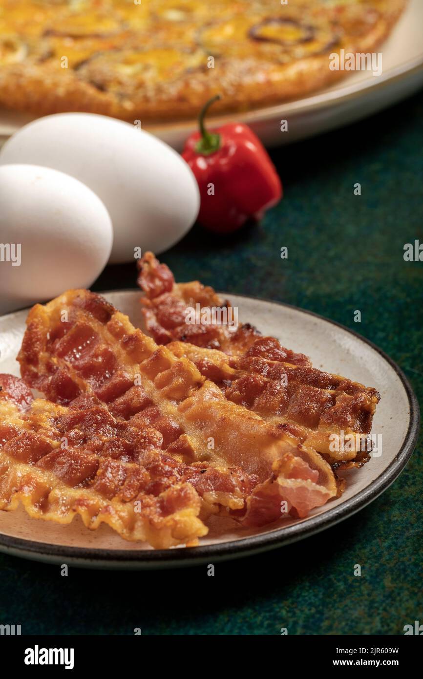 Primo piano di alcune fette croccanti di pancetta e tre uova fresche sullo sfondo. Foto Stock