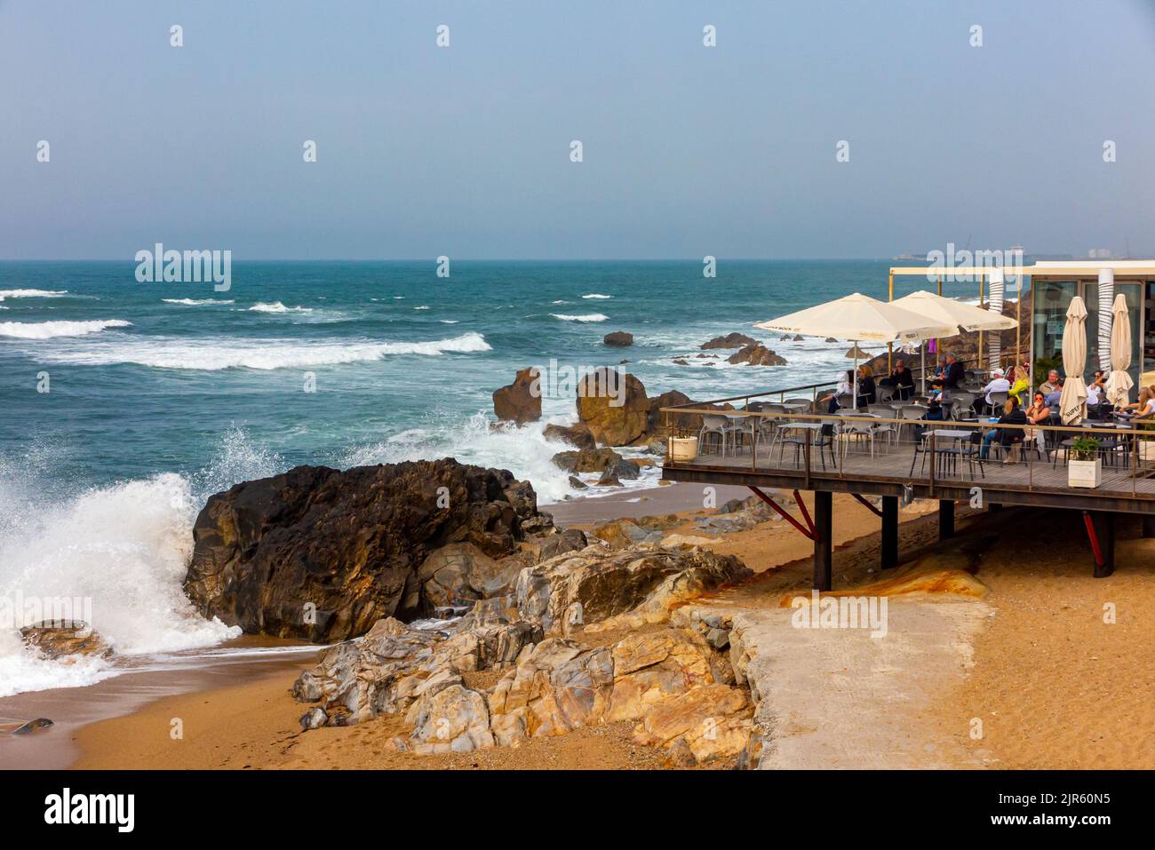 Onde che si schiantano su una spiaggia vicino a un caffè e bar sulla costa atlantica a Foz do Douro vicino a Porto, nel nord del Portogallo. Foto Stock