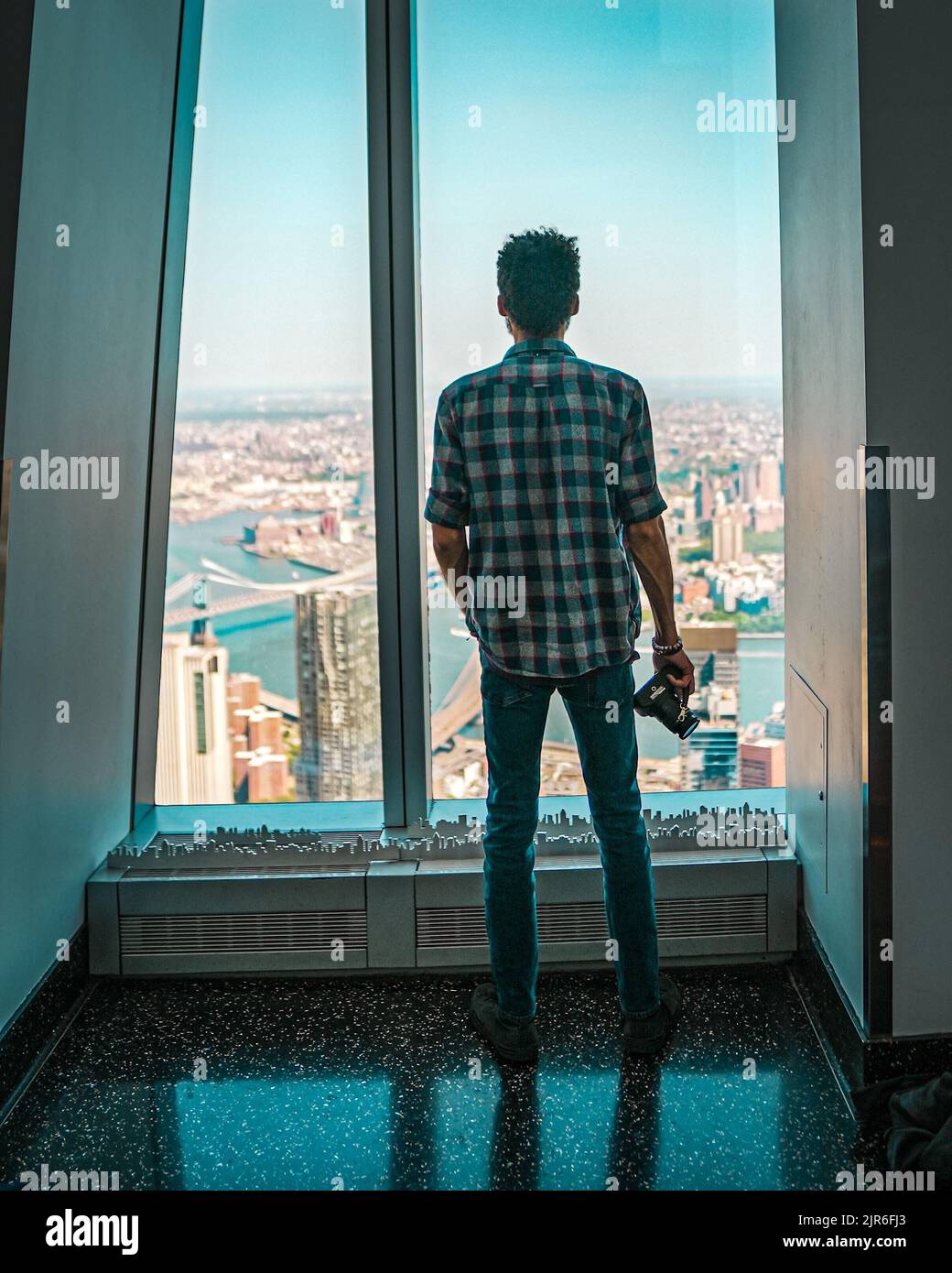 Un giovane uomo in piedi con una macchina fotografica e guardando fuori da una finestra presso l'One World Observatory Foto Stock